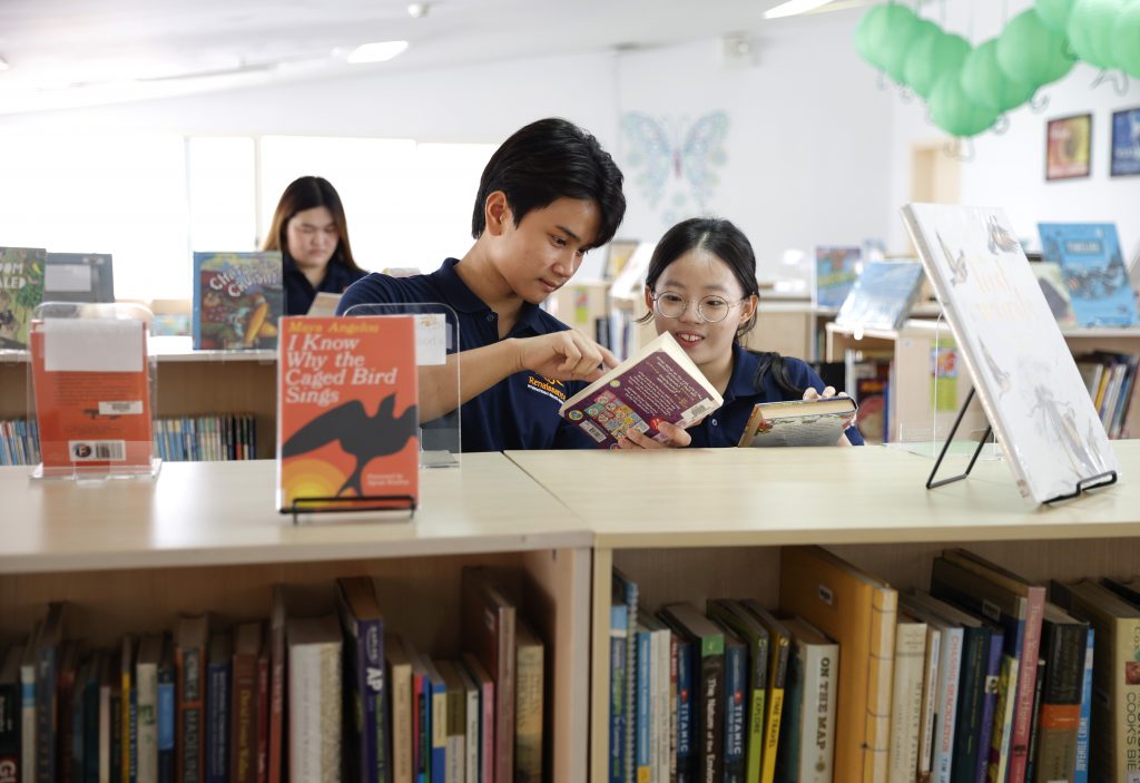 2 secondary students looking at a book smiling happily